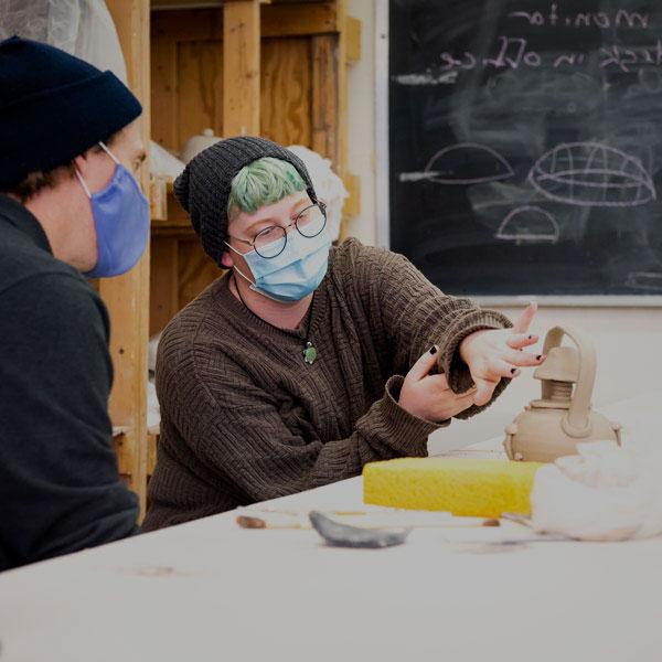 A ceramics student discusses their work with their professor.